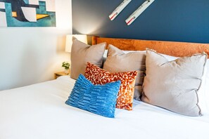 Una cama con varias almohadas, una lámpara y una obra de arte en la pared.