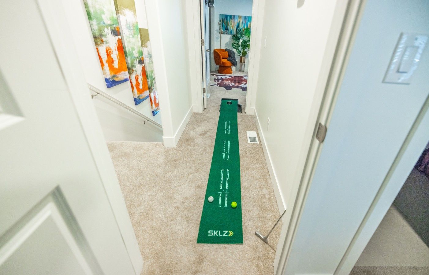 Un couloir avec un tapis de golf vert de la marque SLKZ et une porte blanche.