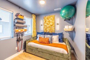 A bedroom with a bed, exercise ball, wall-mounted shelf, and exercise equipment.