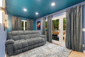 Een woonkamer met een grijze bank, een blauwe wand en een groot raam met gordijnen.