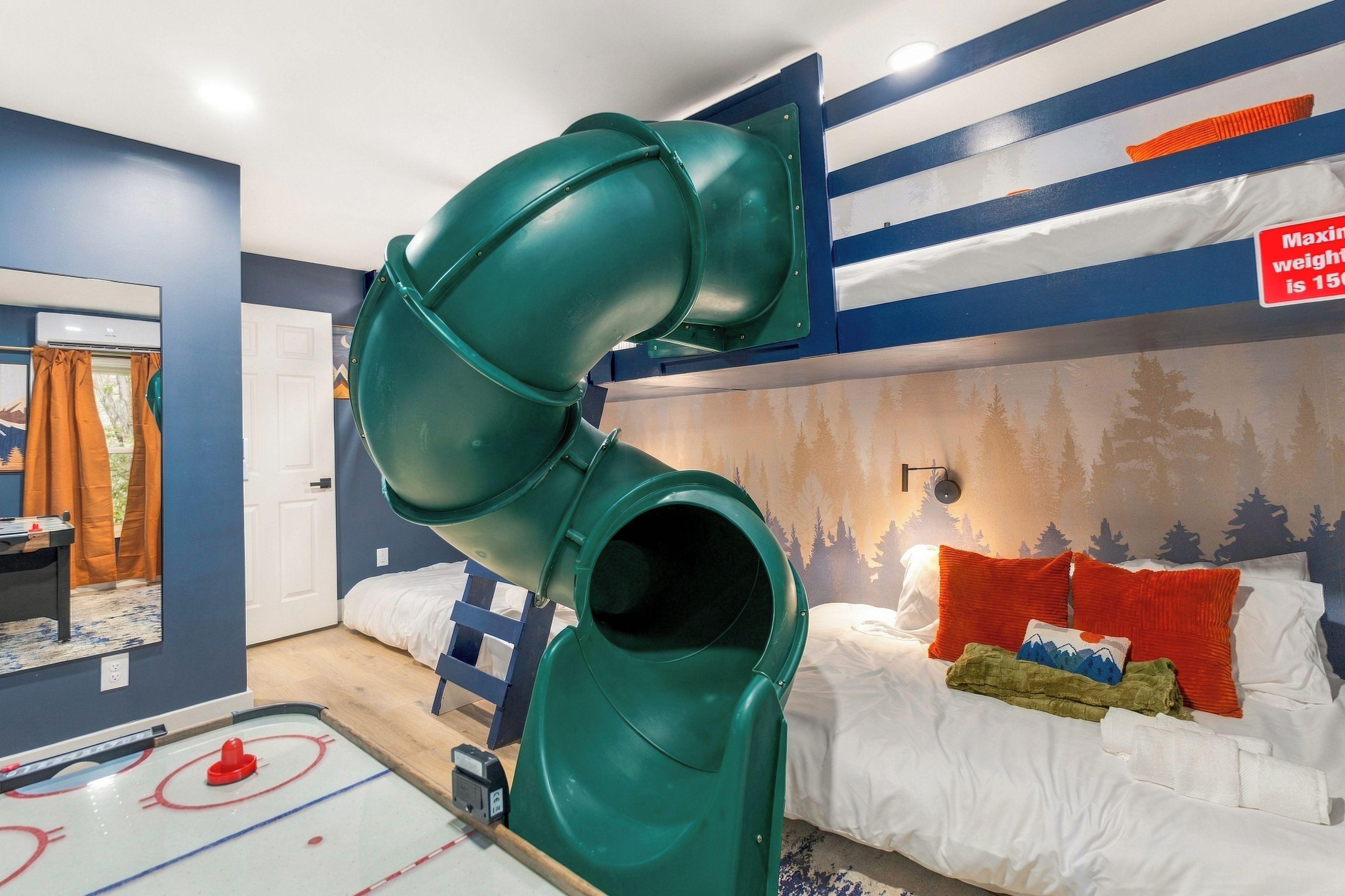 A room with a green slide, a bed with white bedding, and a hockey table.