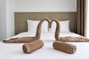 A neatly made bed with a headboard, pillows, and a towel arranged in a heart shape.
