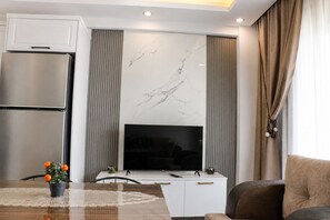 A modern living room with a flat-screen TV mounted on a wall with a marble-like design, a white cabinet below, and a dining table with a vase of flowers.