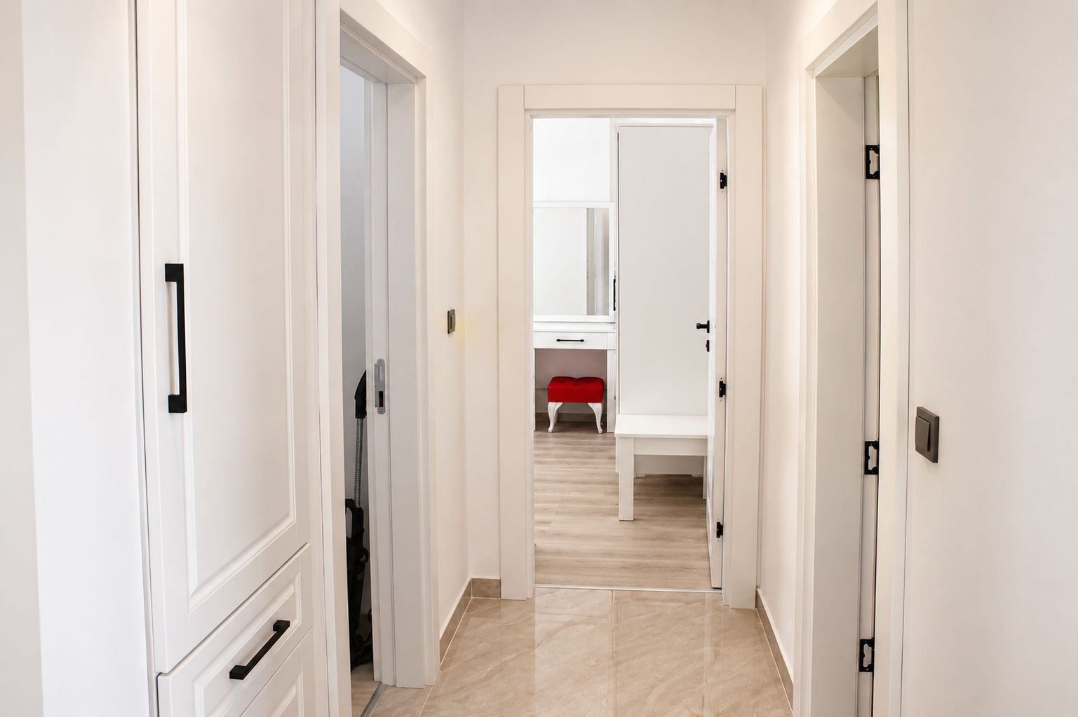 A hallway with white doors, a red bench, and a mirror on the wall.
