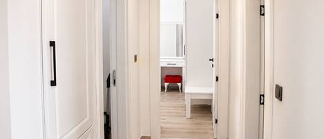 A hallway with white doors, a red bench, and a mirror on the wall.