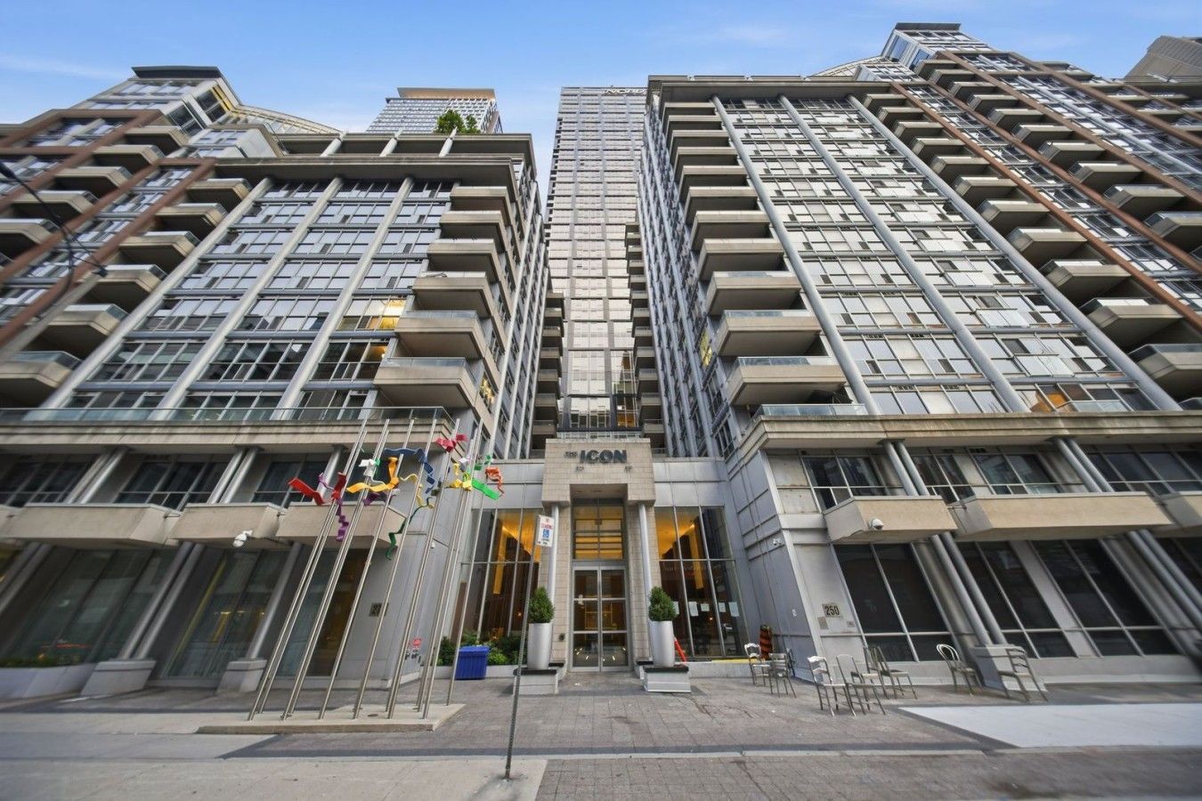 A modern high-rise building with a prominent entrance, multiple balconies, and a clear sky.
