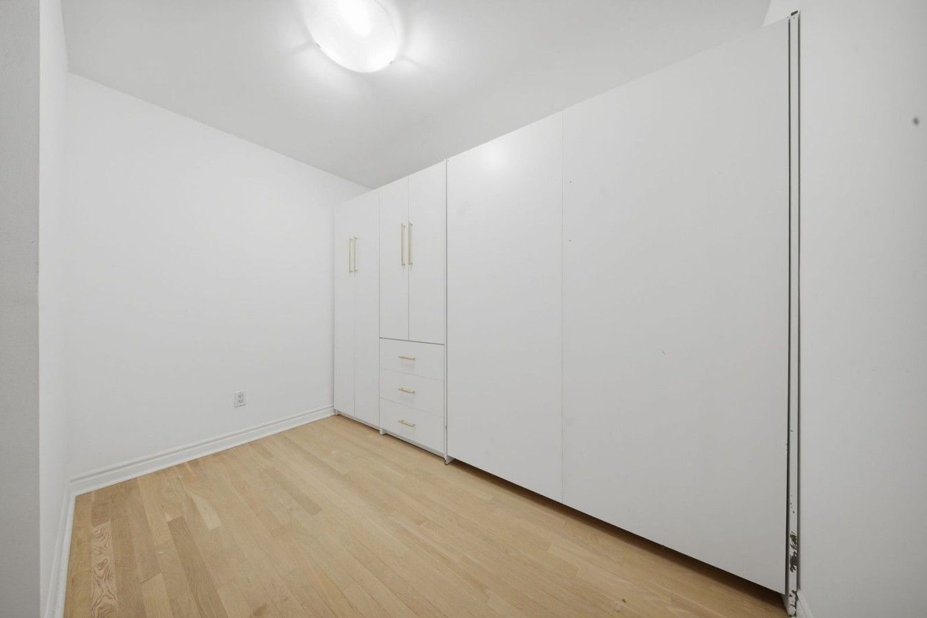 A room with a wooden floor, white walls, and a wardrobe with multiple drawers and doors.