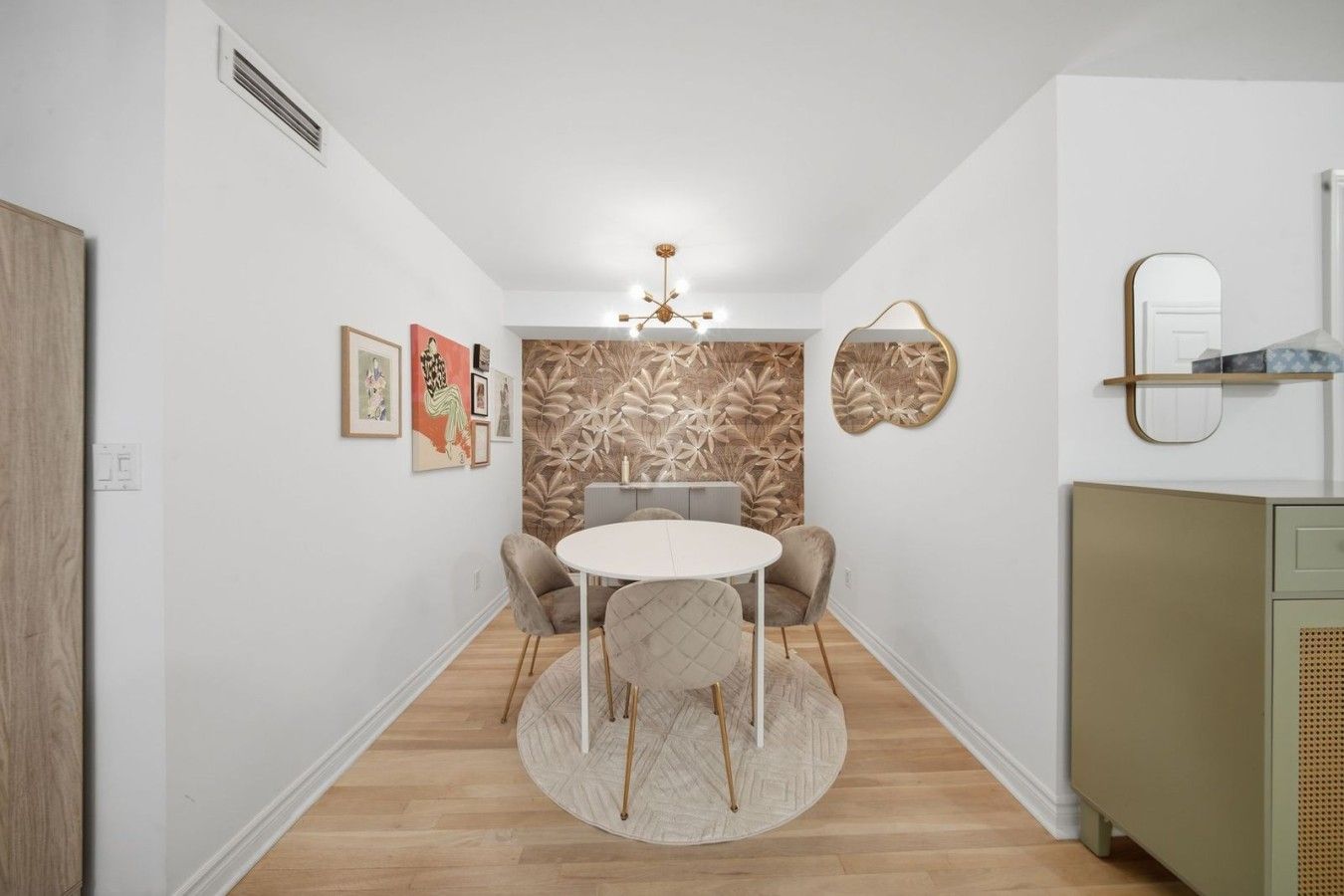 A narrow hallway leading to a dining area with a round table and chairs, a decorative wall with leaf patterns, and a ceiling light fixture.