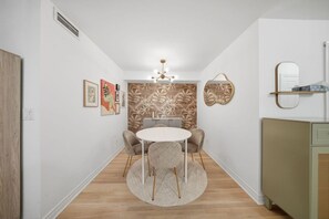 Een smalle gang die leidt naar een eetruimte met een ronde tafel en stoelen, een decoratieve muur met bladmotieven en een plafondlamp.