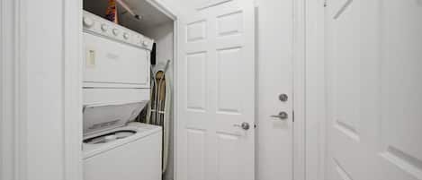 A laundry room with a washer and dryer, a door, and a small shelf with items.