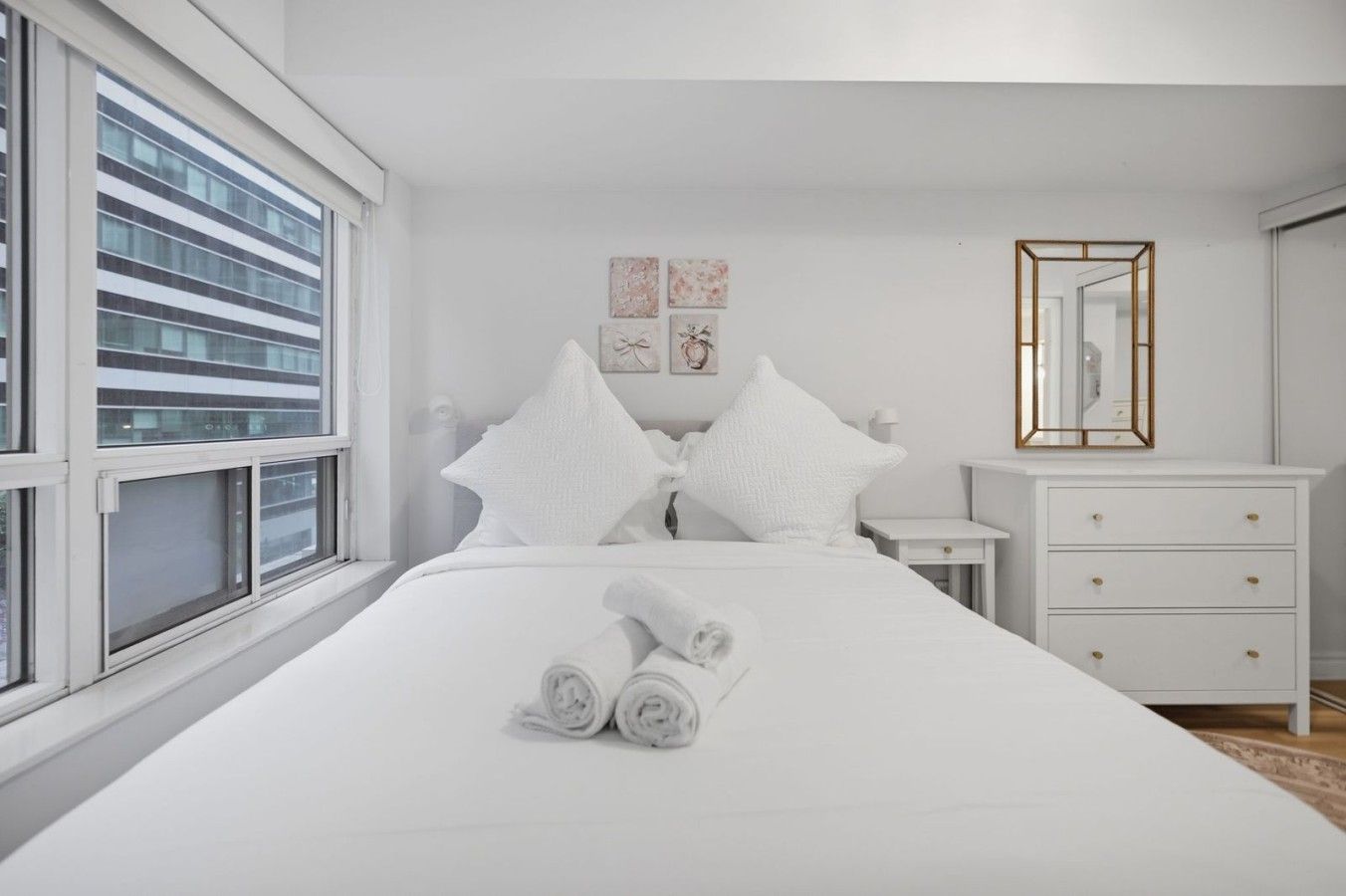 A hotel room with a large bed, a bedside table, a dresser, a mirror, and artwork on the wall.