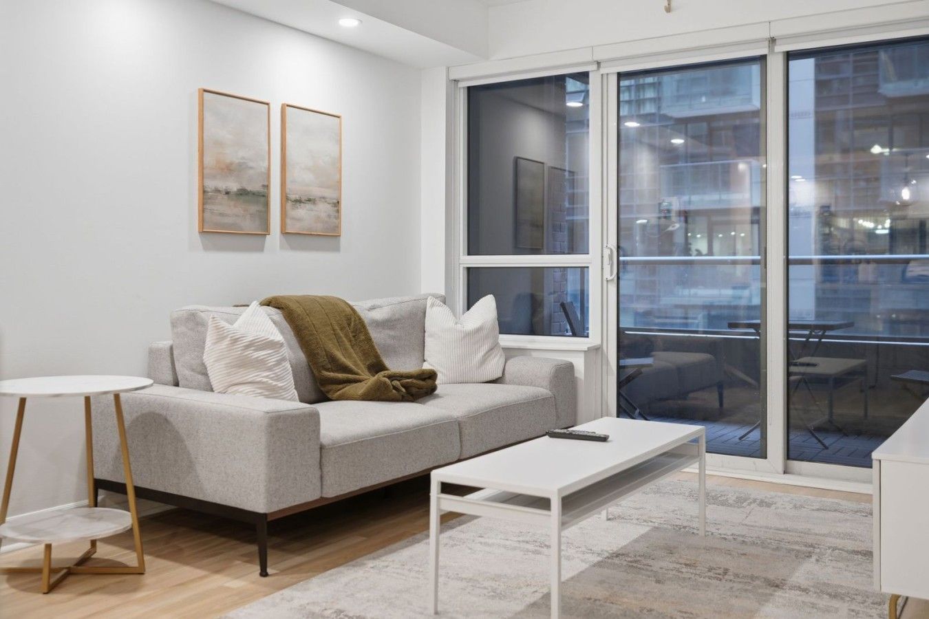 A modern living room with a grey sofa, a white coffee table, and a small round table with a wooden base.