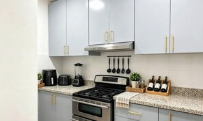 A kitchen with grey cabinets, a stainless steel range hood, a gas stove, a coffee maker, a blender, a toaster, and a wine rack. - El Limoncito Benerito Apartment – Your Caribbean Getaway (San Rafael de yuma)