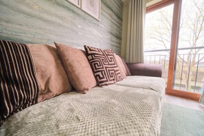 A sofa with patterned cushions in a room with a large window and a view of the outdoors.