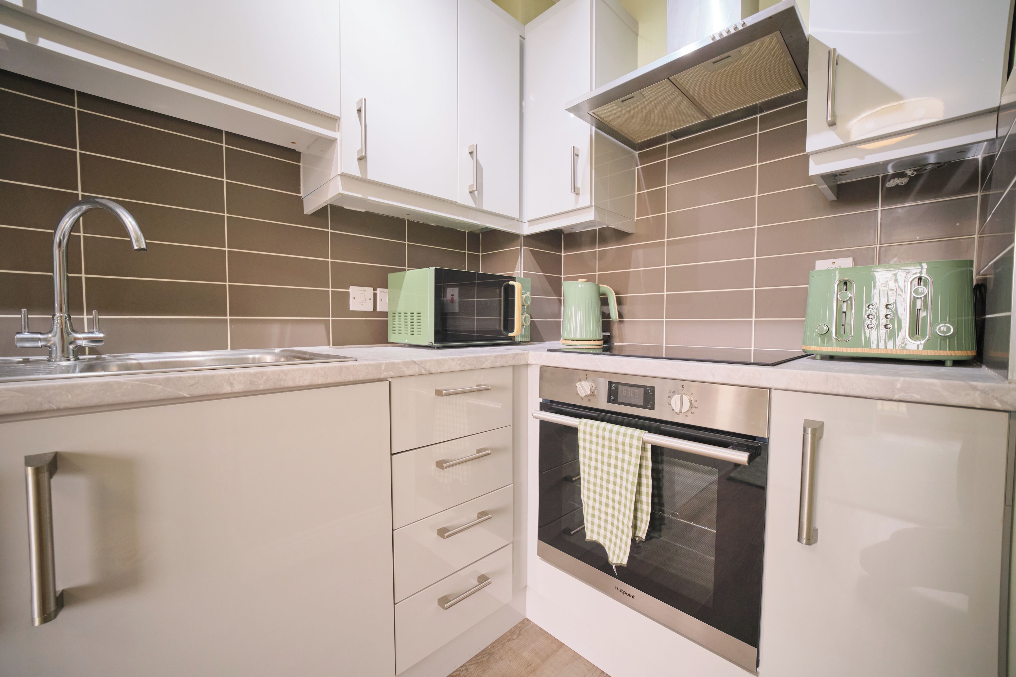 Una cucina con mobili bianchi, un lavello in acciaio inossidabile, un forno a microonde, un bollitore e un forno.