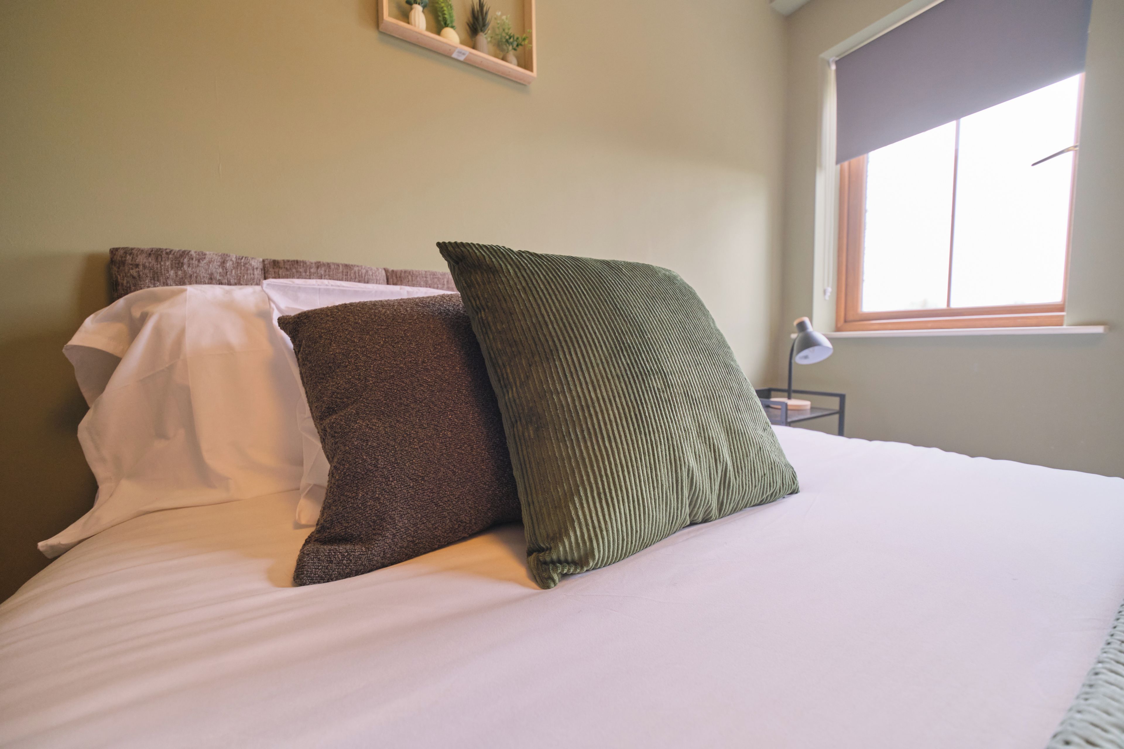 A bed with white bedding and three pillows of different textures and colors.