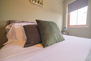 A bed with white bedding and three pillows of different textures and colors.