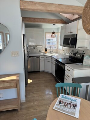 A modern kitchen with white cabinets, stainless steel appliances, and a wooden ceiling.