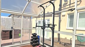 A gym with a pull-up bar and weight rack, large windows, and a view of a backyard. - Independent, Modern Annexe in Orpington (Orpington)