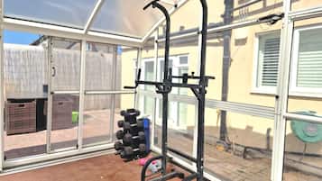 A gym with a pull-up bar and weight rack, large windows, and a view of a backyard.