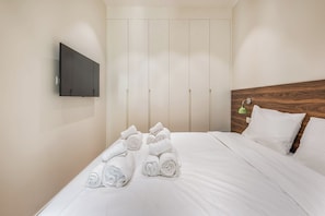 Ein Hotelzimmer mit einem Bett, einem an der Wand befestigten Fernseher und einem hölzernen Kopfteil.