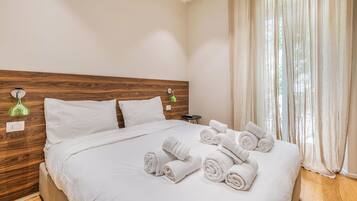 Een hotelkamer met een houten hoofdeinde, een bed met witte lakens, een groene wandlamp en een raam met dunne gordijnen.