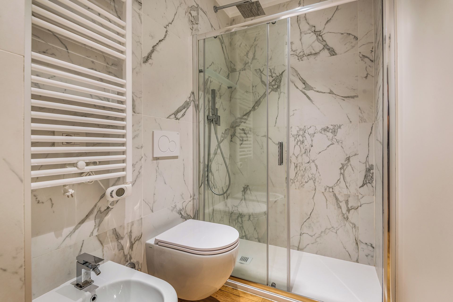 A modern bathroom with a glass-enclosed shower, a toilet, and a bidet.