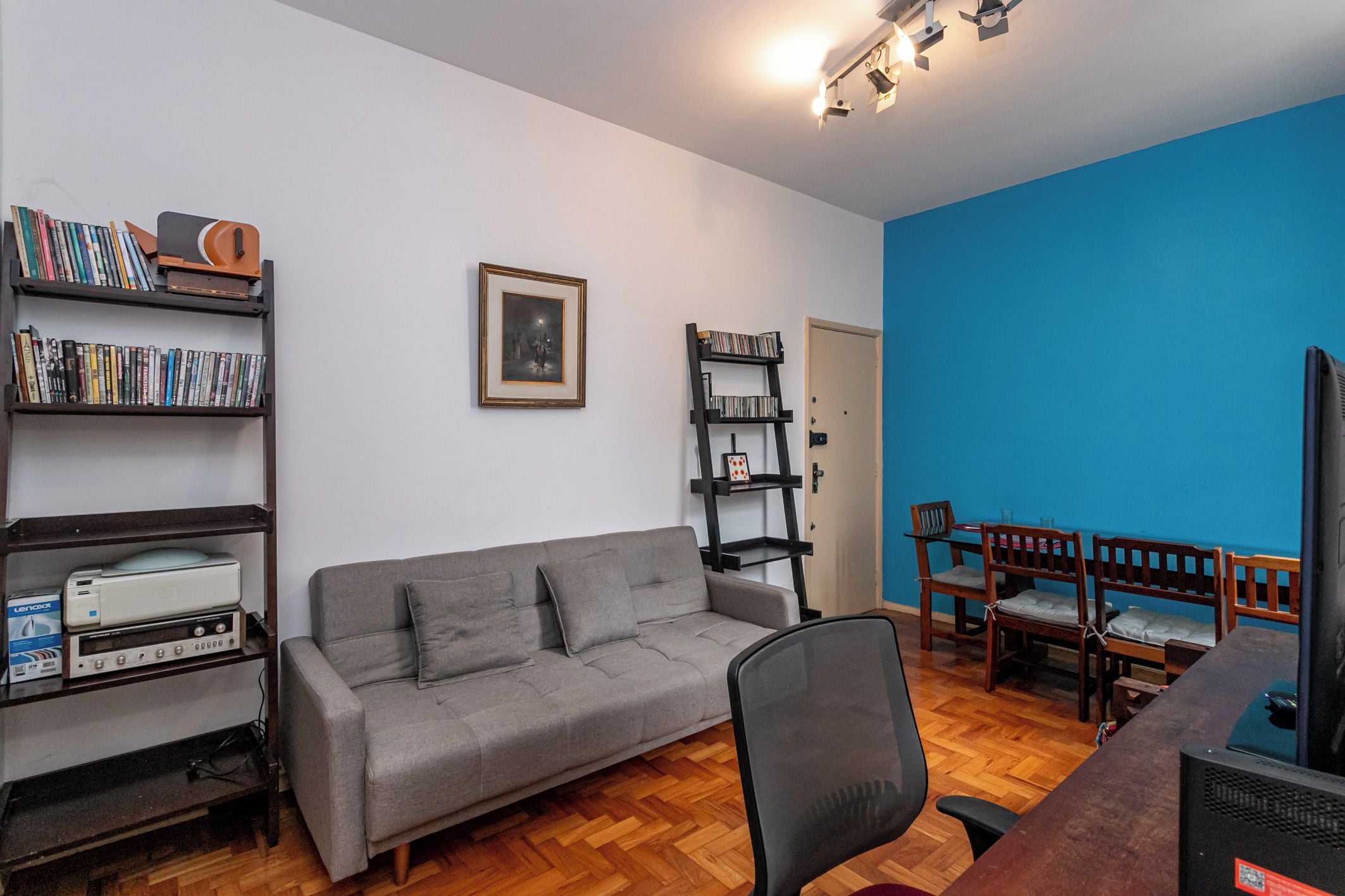 Un salon avec un canapé gris, une bibliothèque, un tableau encadré au mur et un mur d’accent bleu.