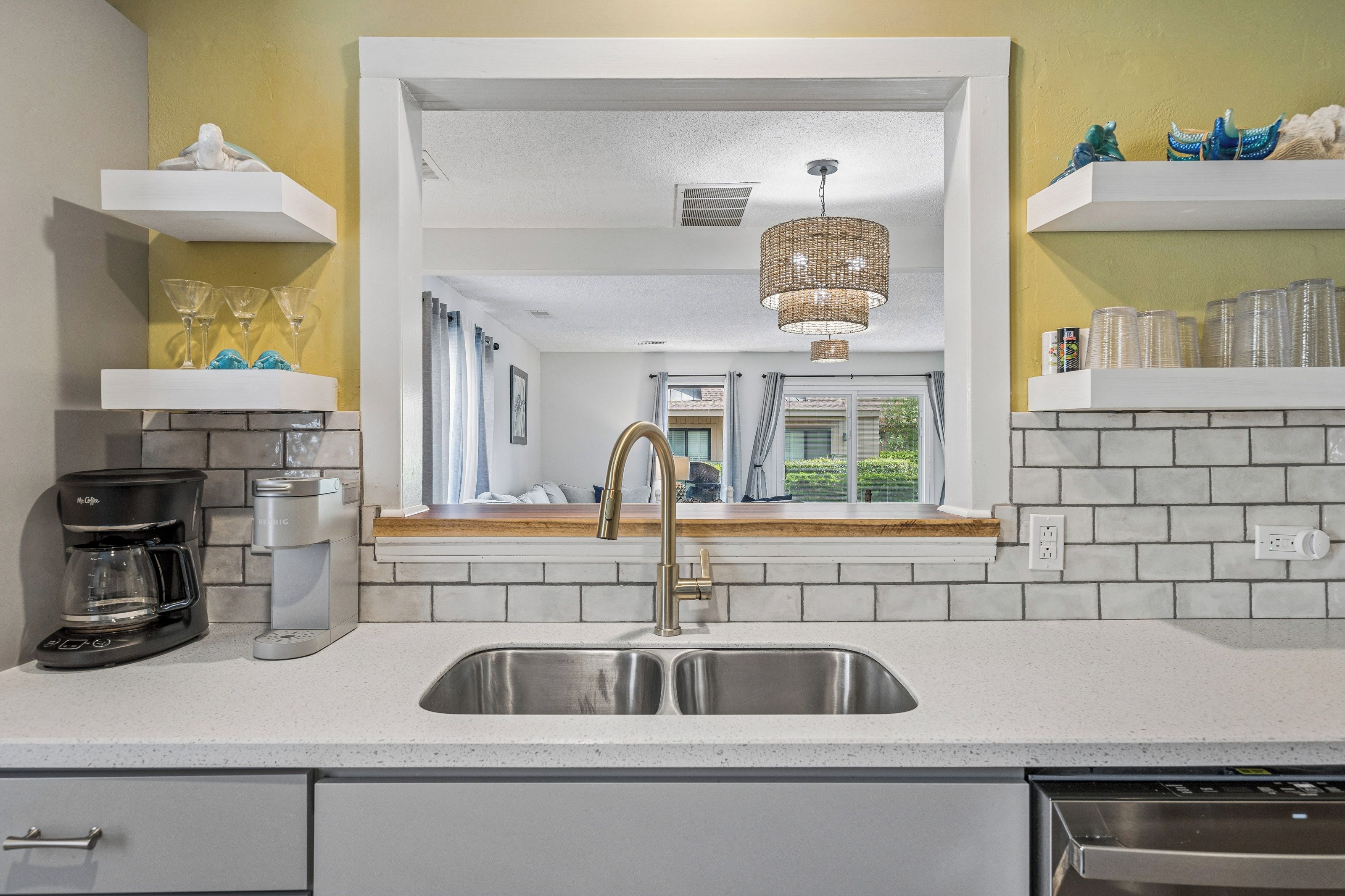 A kitchen with a stainless steel sink, a coffee maker, and a window with a view of the outside.