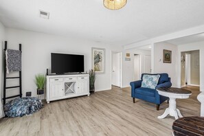 Ein Wohnzimmer mit Flachbildfernseher, einem blauen Sofa, einem weißen Schrank und Holzboden.