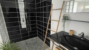 Un baño con paredes de azulejos negros, ducha, lavamanos, espejo y escalera de madera.