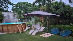 Un patio trasero con un jacuzzi de madera, un tobogán, sillas de descanso, una mesa con una planta y una pérgola con sombrilla.