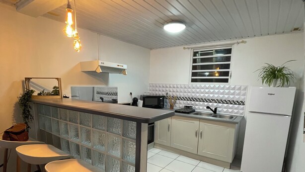 Una cocina con barra, armarios blancos, microondas y refrigerador.