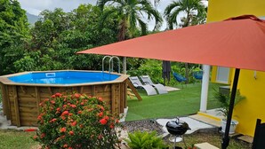 Un patio con un jacuzzi de madera, un paraguas rojo y un jardín con flores rojas.