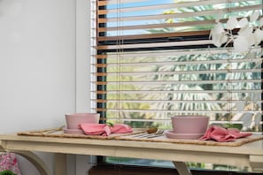 A dining area with a table set for two, featuring pink plates and napkins, and a window with horizontal blinds. - Farm Stay, 5beds / 4.5 baths, Palm Tree, Alpaca & Llama Farm, 5 Acres (West Palm Beach)