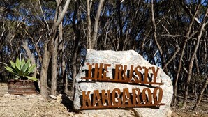 A large rock with 'The Rusty Kangaroo' engraved on it, surrounded by trees.