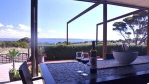 An outdoor patio with a table, two wine glasses, and a bottle of wine.