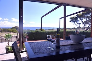 An outdoor patio with a table, two wine glasses, and a bottle of wine.