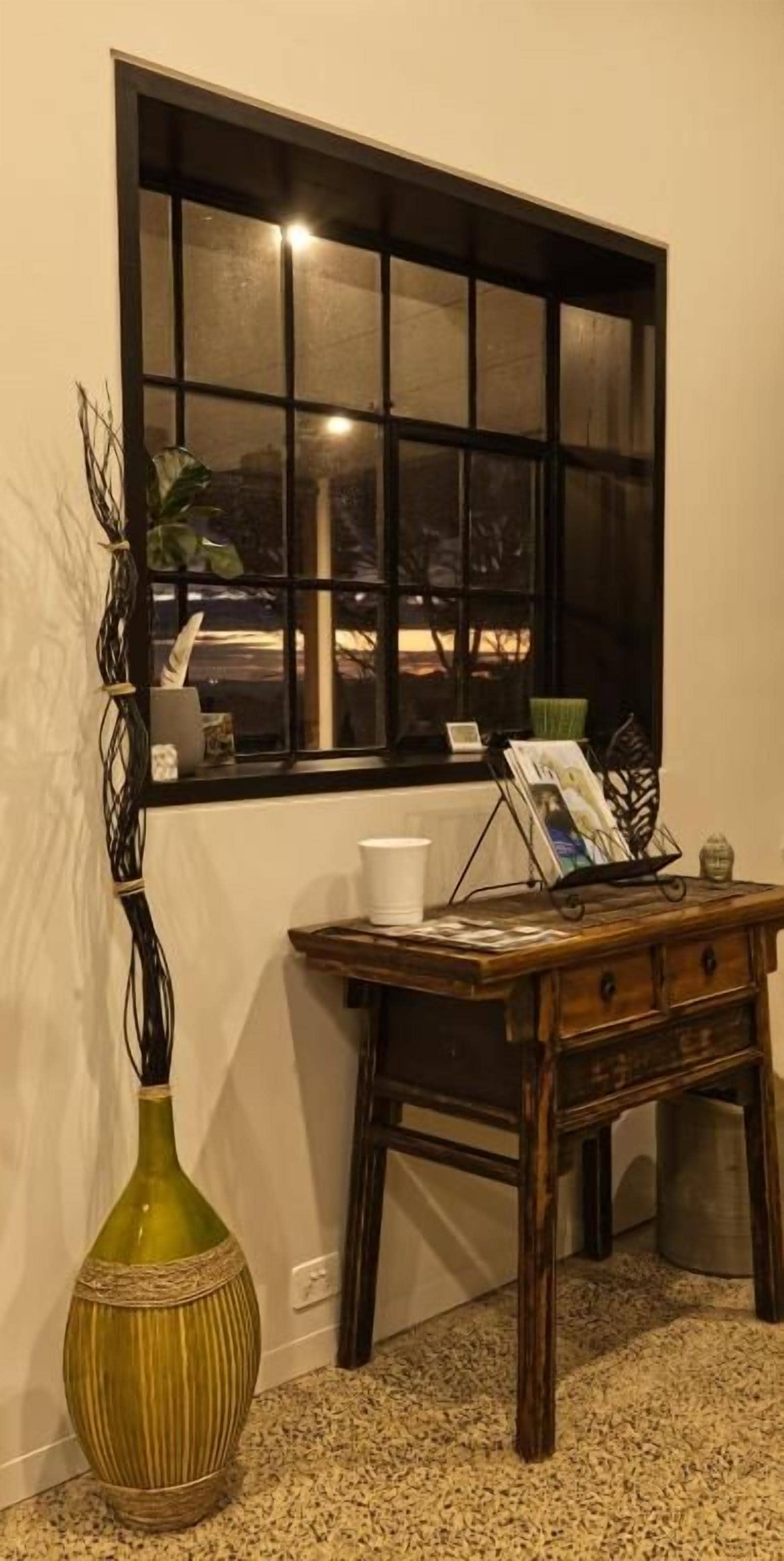 A room with a window, a wooden desk, a green vase, and a white cup.