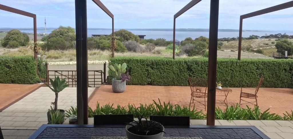 A patio with a view of the sea, potted plants, and outdoor furniture.