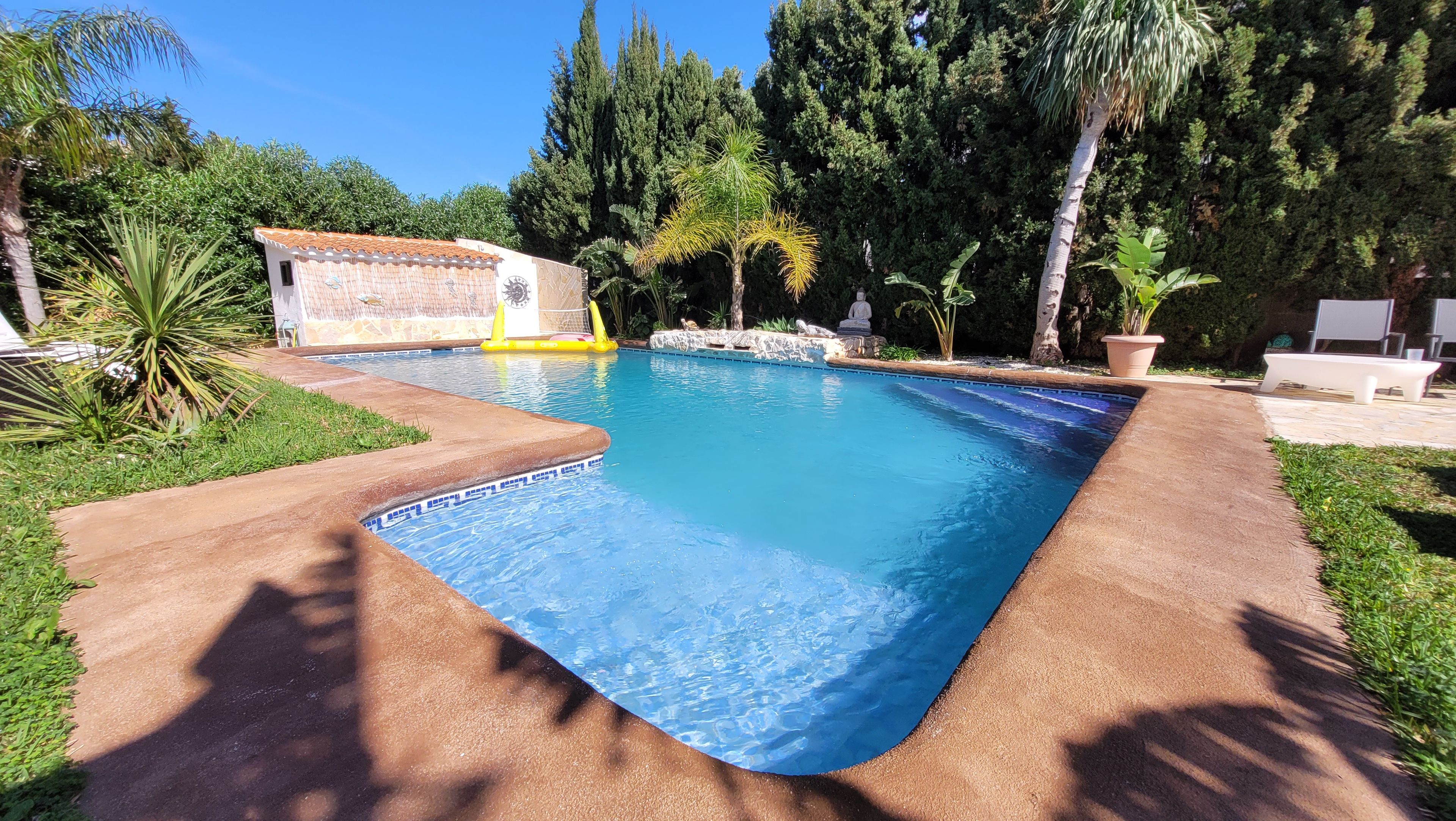 A swimming pool with a tiled edge, surrounded by grass and trees.