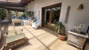 An outdoor patio with wooden flooring, a sofa, a chair, a table with a decorative centerpiece, and potted plants. - Large villa near the city and the beach, with a pool, hot tub, and saunas, offering plenty of space for 14 people (Dénia)