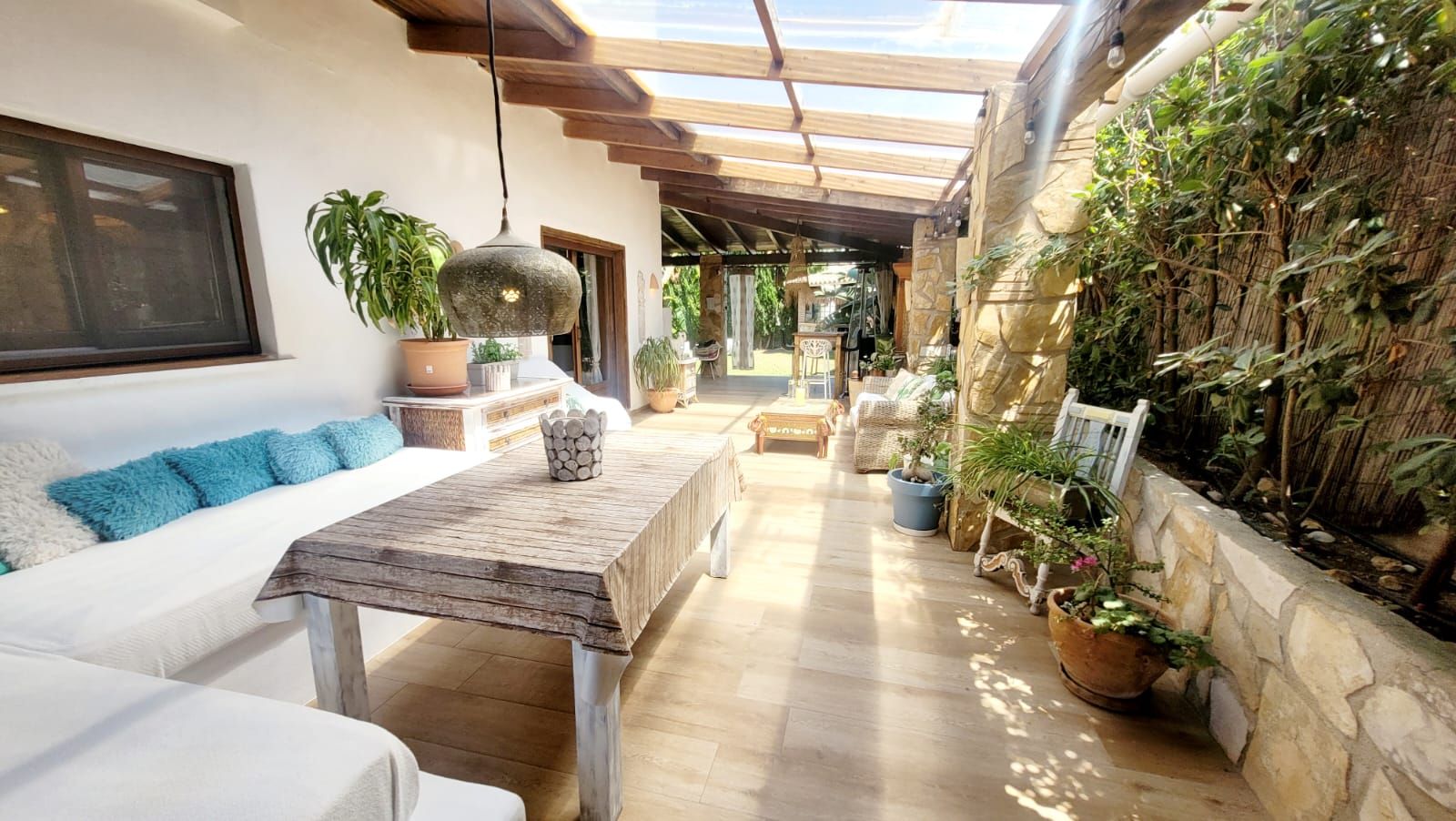 A sunlit interior with a wooden table, white sofa, and potted plants.
