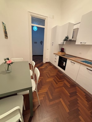 A compact kitchen with white cabinets, a wooden herringbone floor, and a dining area with a table and chairs. - Jesshouse – In the heart of Palermo, combining comfort and city life (Palermo)