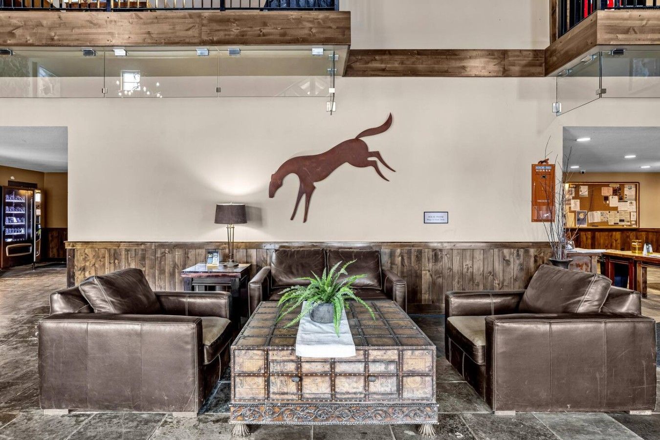 A lobby with leather sofas, a decorative wall, a wooden coffee table, and a vending machine.