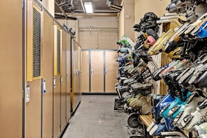 A narrow hallway with lockers on one side and a wall of stacked helmets and motorcycle gear on the other.