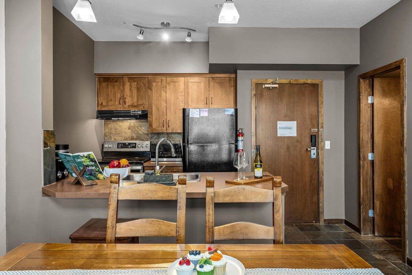 A modern kitchen with wooden cabinets, a black refrigerator, and a dining area with a wooden table and chairs.