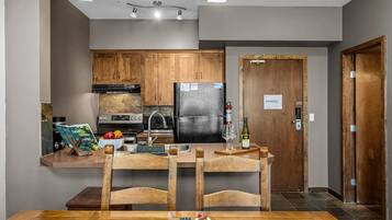 A modern kitchen with wooden cabinets, a black refrigerator, and a dining area with a wooden table and chairs.