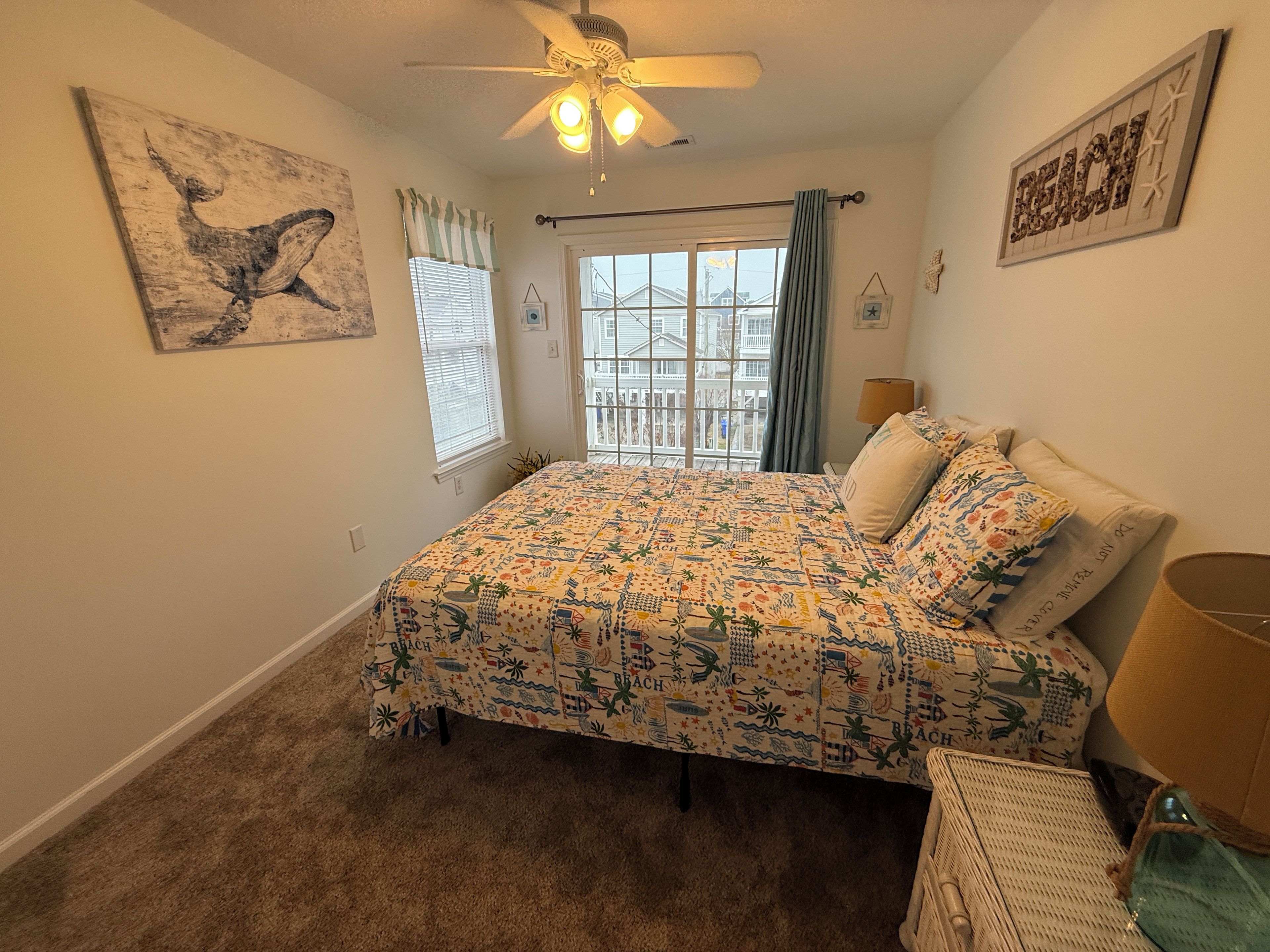 A bedroom with a bed, a ceiling fan, a window with curtains, and artwork on the walls.