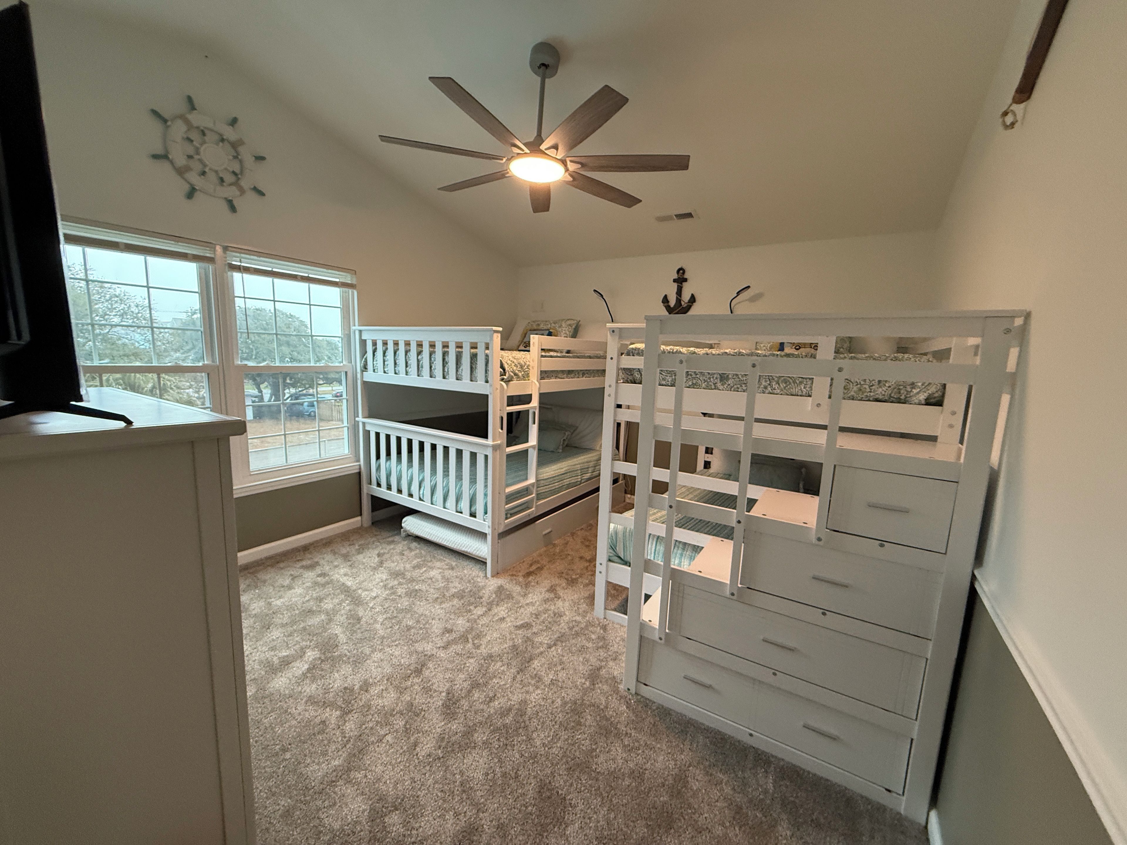 A room with bunk beds, a ceiling fan, a window, and a desk.